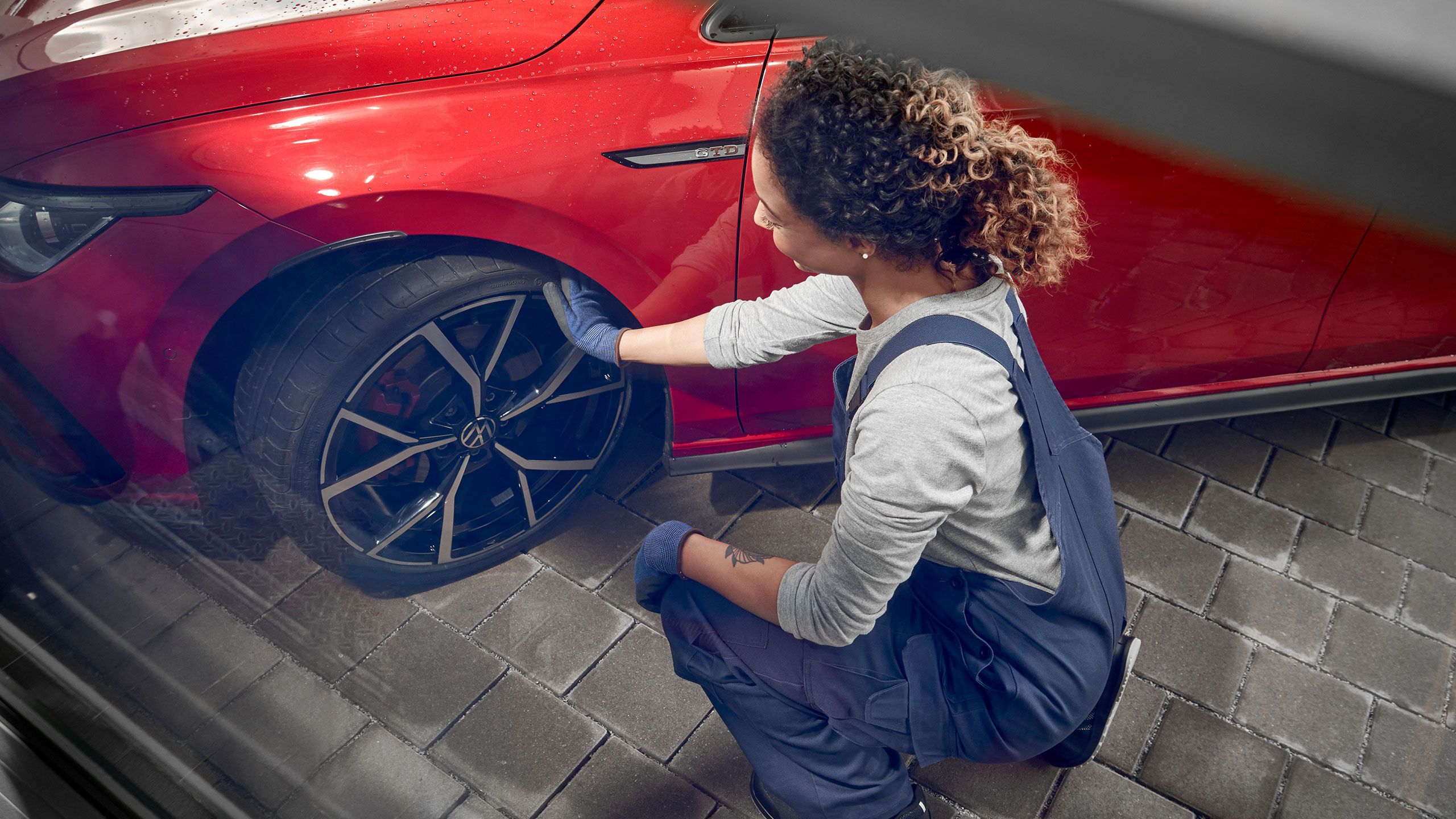 Funcionário de serviço da VW em frente a um Volkswagen vermelho numa oficina