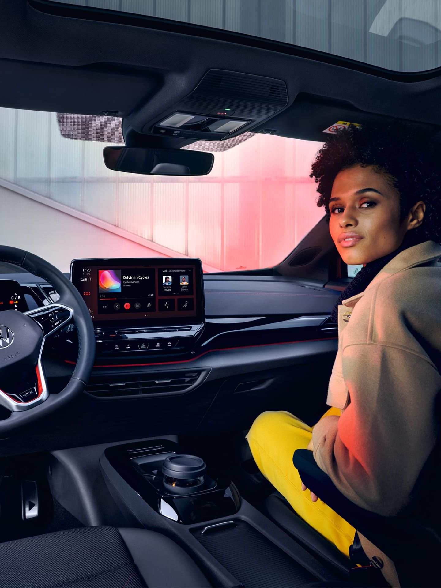 Interior de um VW ID.4 GTX com vista para os bancos dianteiros e cockpit. Mulher sentada no banco do passageiro a olhar para trás.