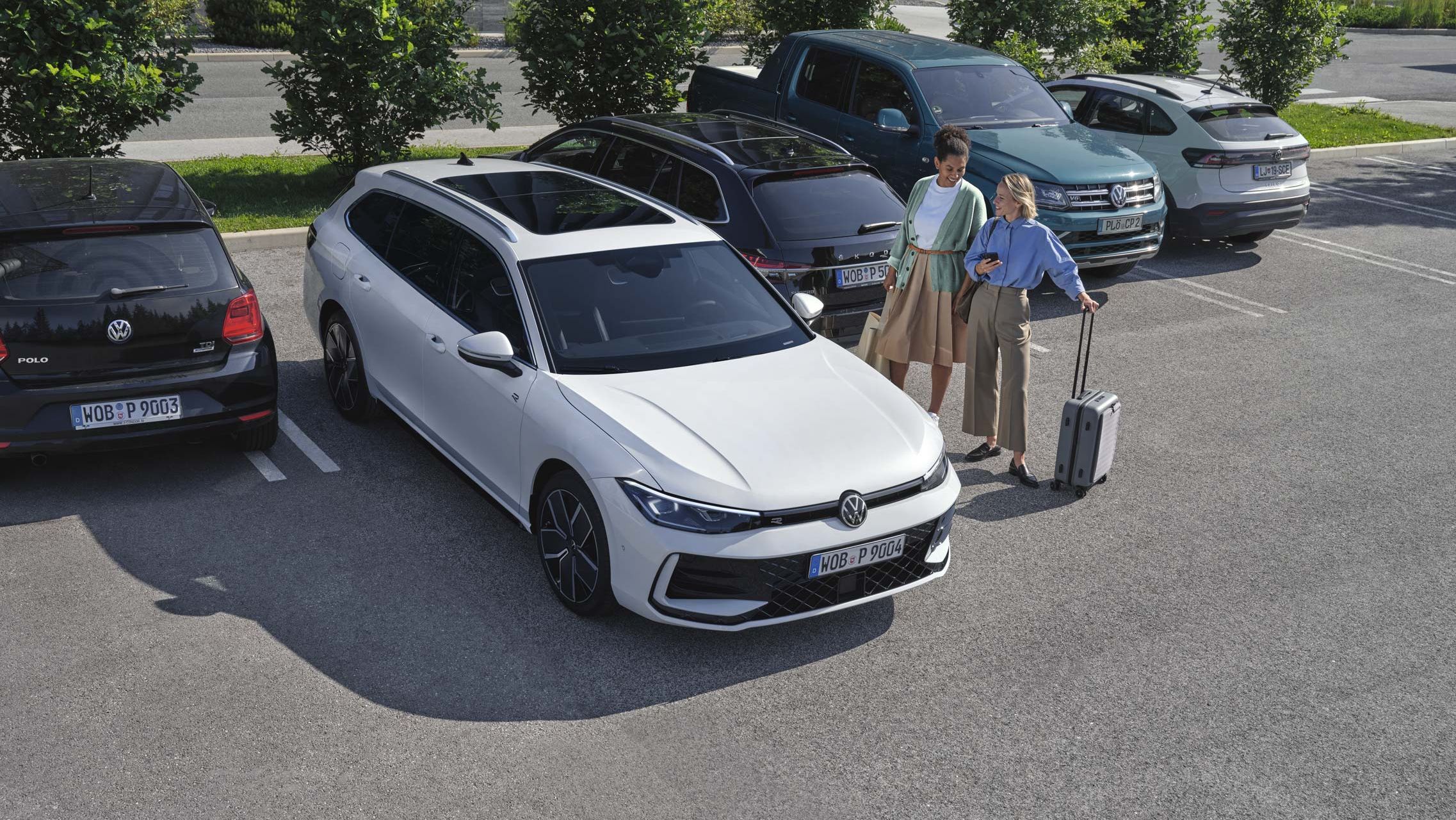 Duas mulheres do lado de fora do VW Passat branco, que estaciona por elas utilizando o sistema opcional Park Assist Plus. Uma mulher segura o seu smartphone na mão.