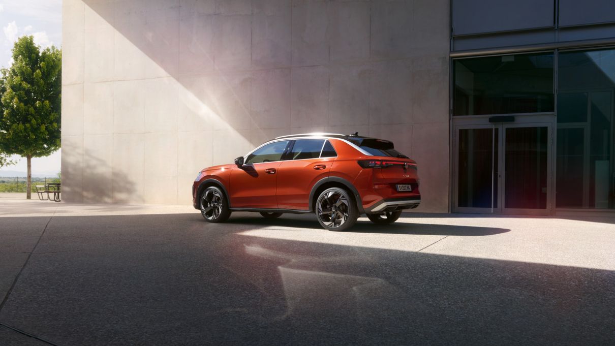 Um VW T-Roc Style vermelho está estacionado em frente a um edifício moderno com arquitetura em betão curvilínea.