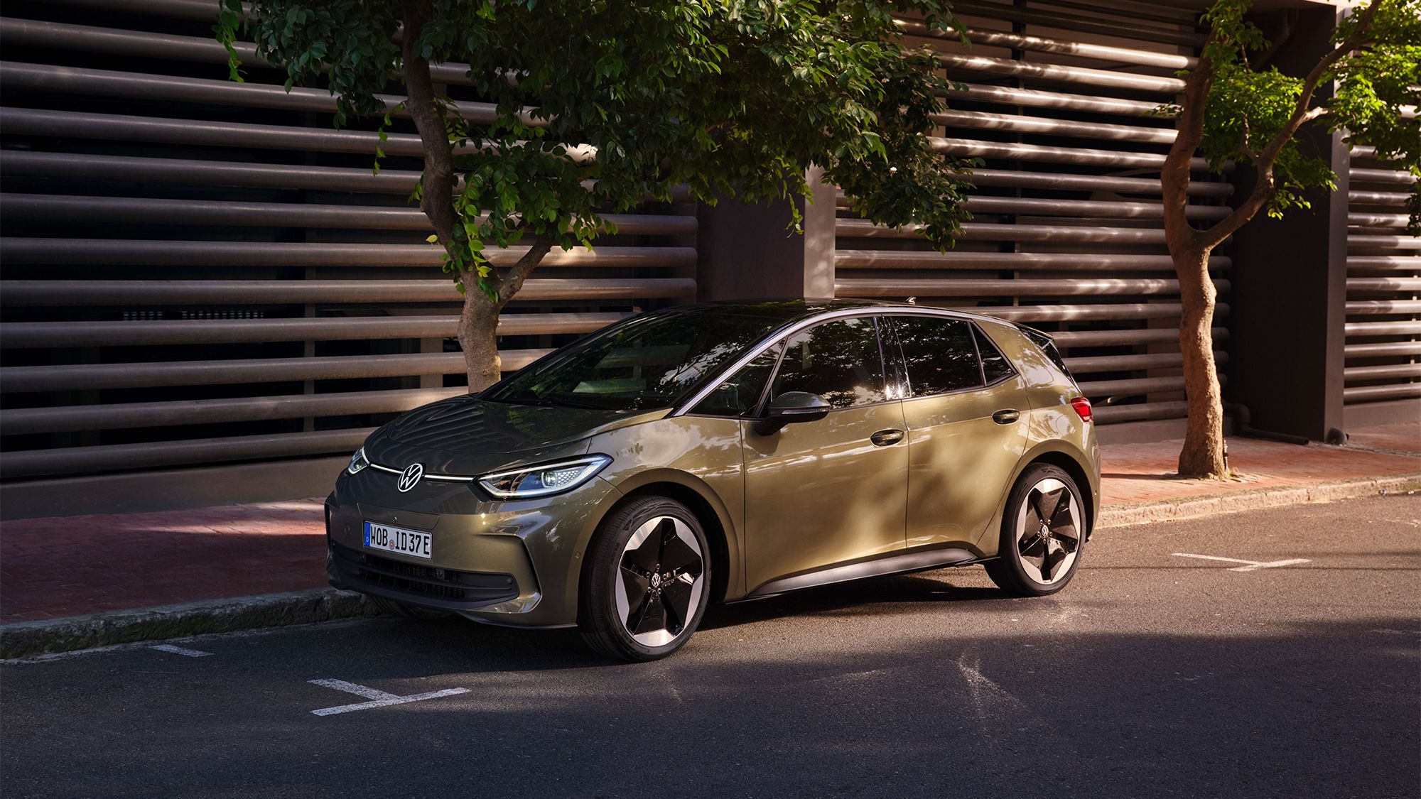 Vista de um VW ID.3 em "Dark Olivine Green Metallic" e jantes "Sanya", estacionado à beira do lancil. 