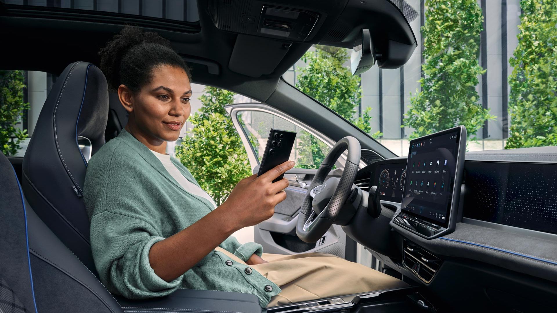 Uma mulher sentada no banco do condutor de um VW Passat estacionado, com a porta aberta, a olhar para o seu smartphone.
