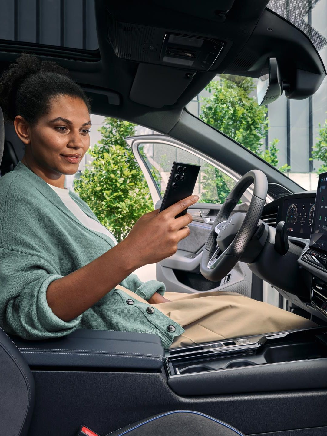 Uma mulher sentada no banco do condutor de um VW Passat estacionado, com a porta aberta, a olhar para o seu smartphone.