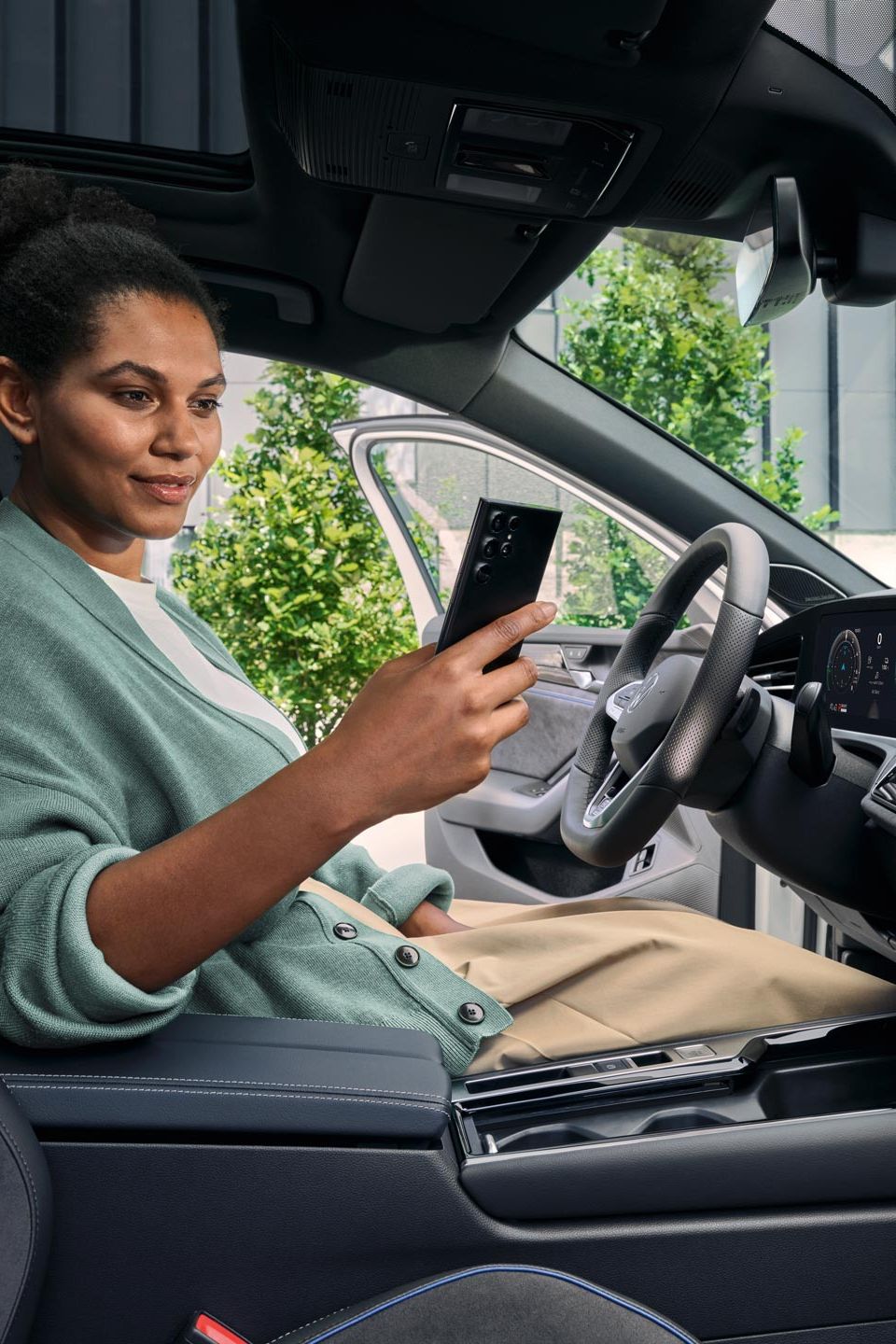 Uma mulher sentada no banco do condutor de um VW Passat estacionado, com a porta aberta, a olhar para o seu smartphone.