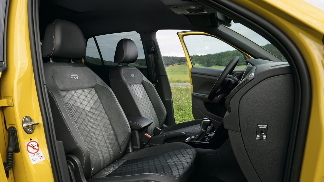 Vista pela porta do passageiro do VW T-Cross amarelo com os bancos Comfort desportivos  e o apoio de braços central.  