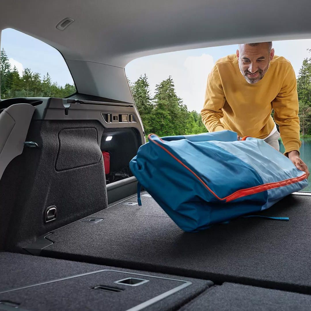 Um homem carrega bagagem no generoso compartimento de carga do VW Passat com os bancos traseiros rebatidos. Vista do interior.