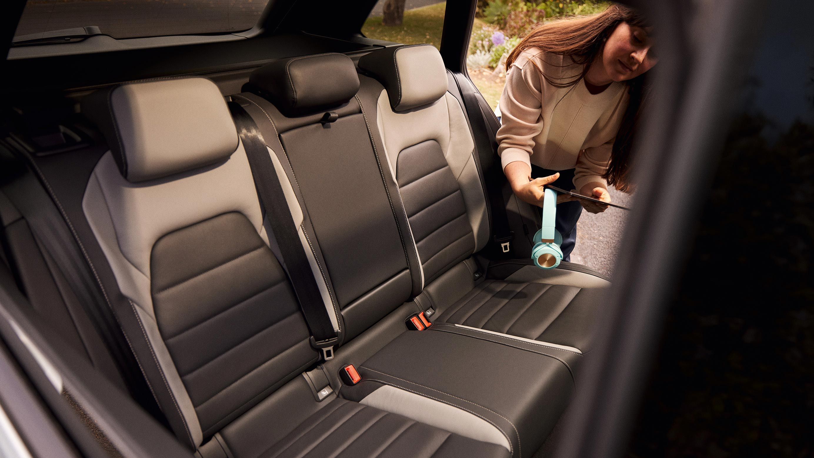 Blick auf die Rückbank des VW Golf Estate. Eine Frau lehnt sich bei geöffneter Tür in den Wagen hinein und hält ein Headset und ein Tablet in der Hand.