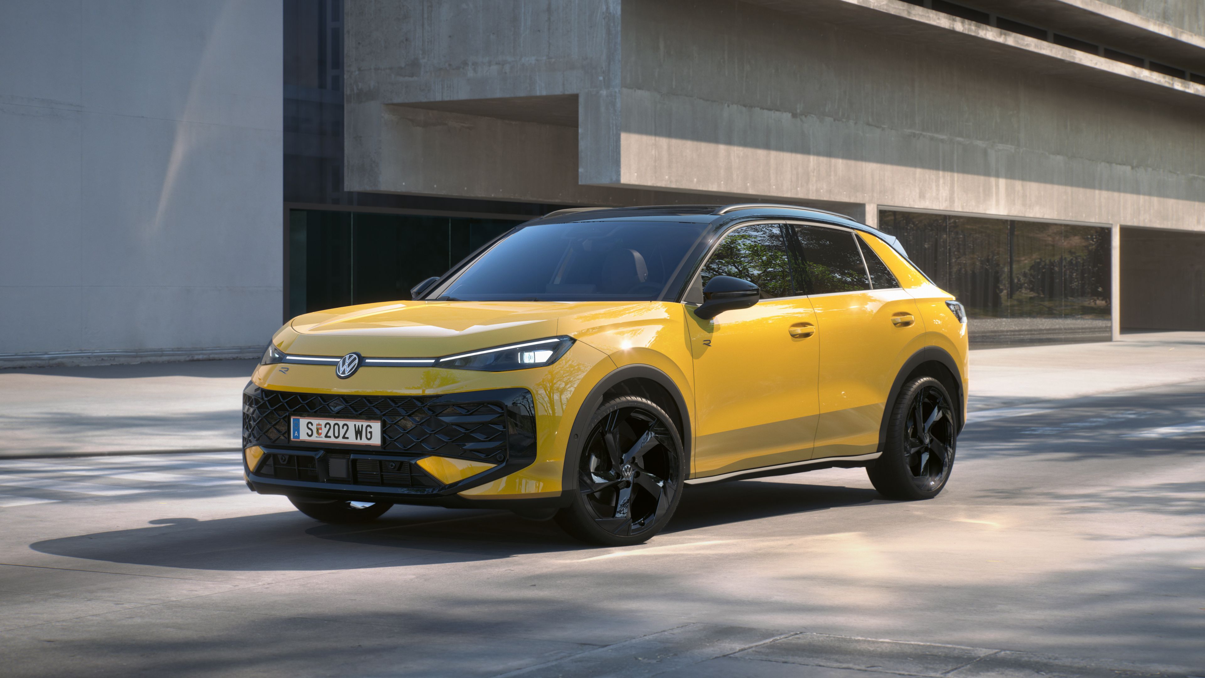 Um Volkswagen T-Roc R-Line amarela está em frente a um edifício em vista frontal de 3/4.