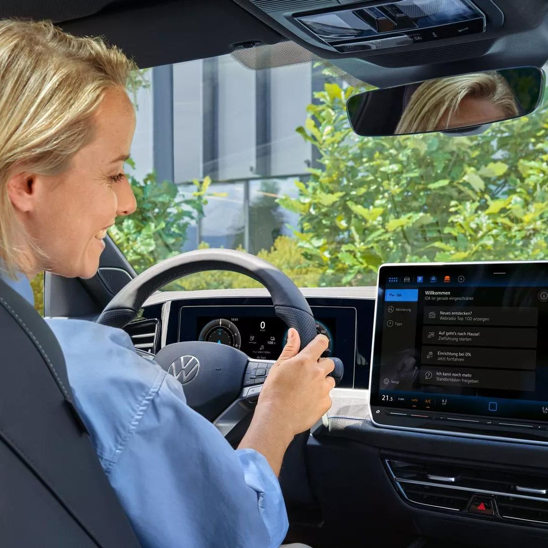 Uma jovem mulher sentada ao volante e a interagir com o assistente de voz do Passat com um sorriso.