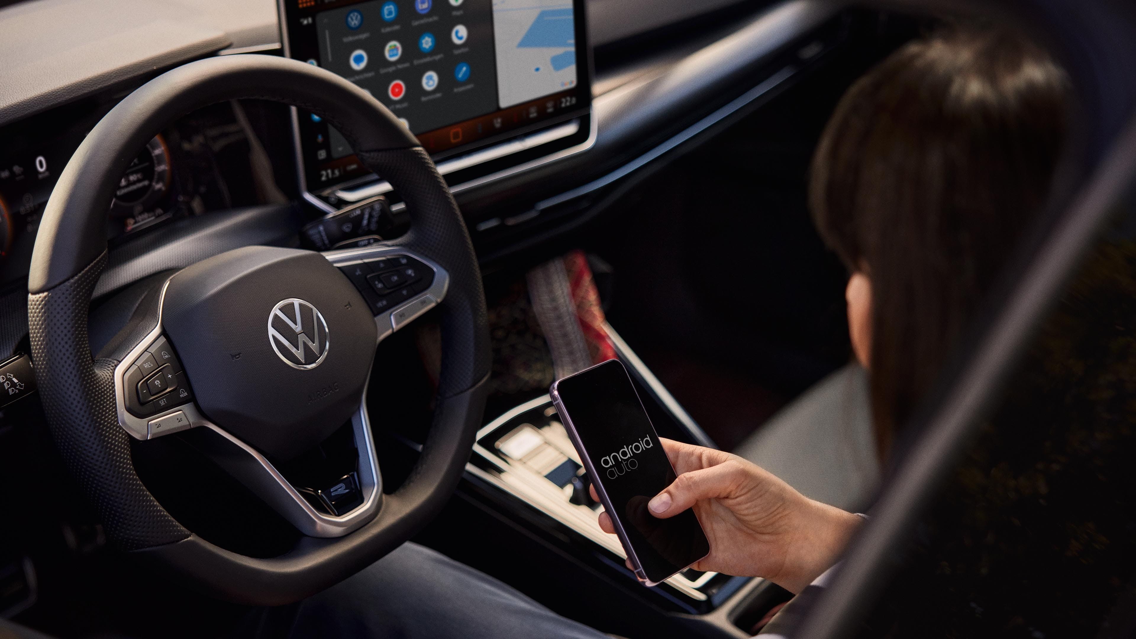 Vista do interior do VW Golf. Uma mulher no banco do condutor utiliza um smartphone para operar o sistema de Infotainment.