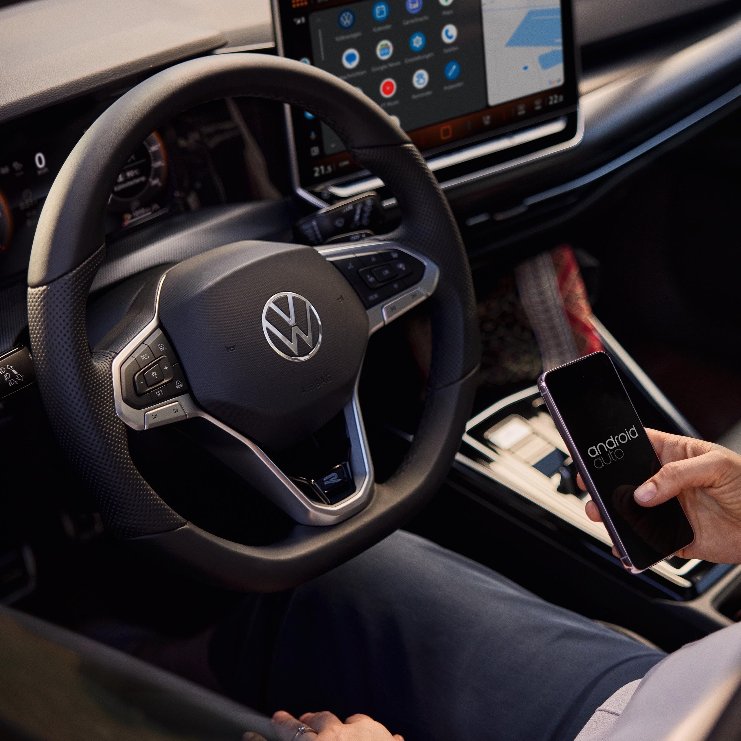 Vista do interior do VW Golf. Uma mulher no banco do condutor utiliza um smartphone para operar o sistema de Infotainment.