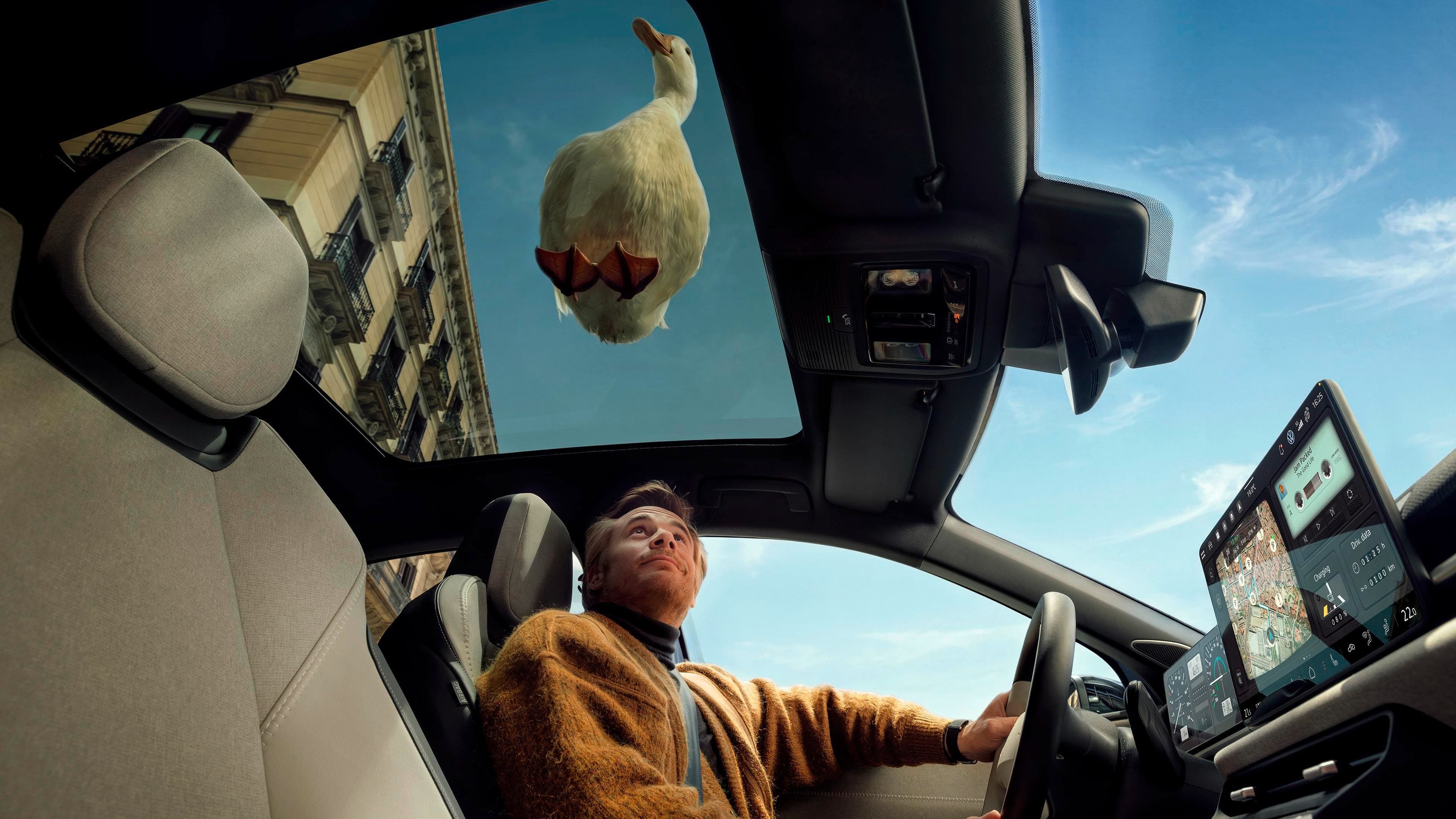 Um homem está sentado no lugar do condutor de um VW ID. Polo e olha para cima, através do teto panorâmico. Um pato branco está pousado sobre o carro.