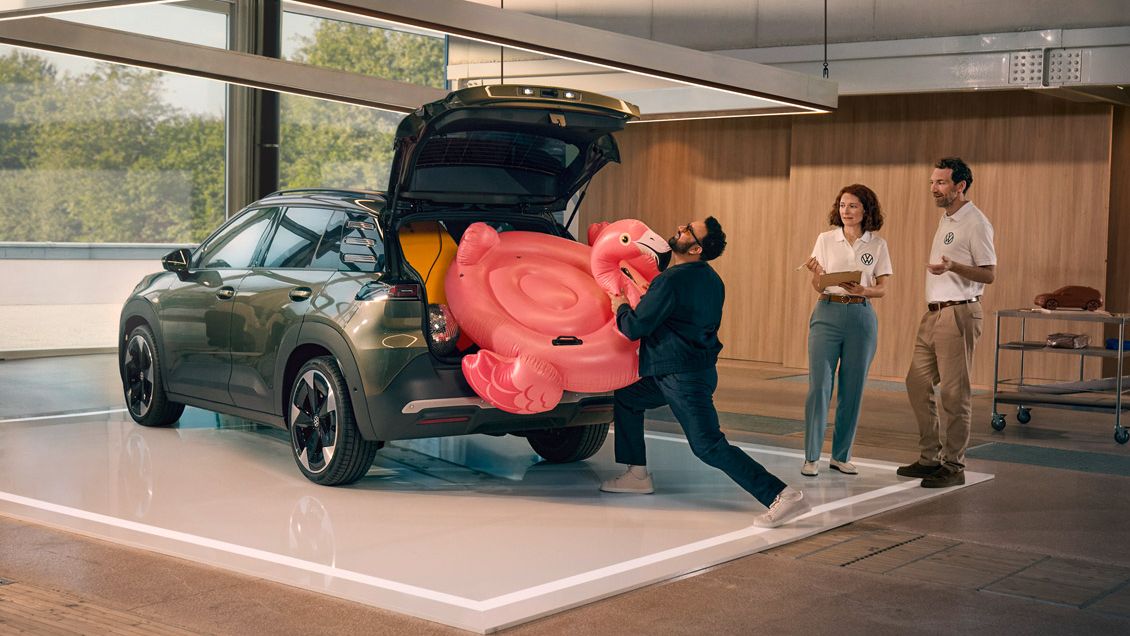 Um homem empurra um flamingo insuflável para dentro da bagageira aberta do VW ID. Cross. Duas pessoas estão ao seu lado e divertem-se a olhar para ele.