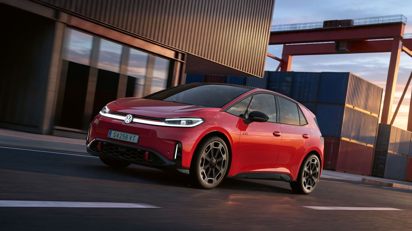 [AI-modified] – Um VW ID.3 GTI vermelho passa por um edifício portuário com os faróis ligados e o logótipo iluminado.