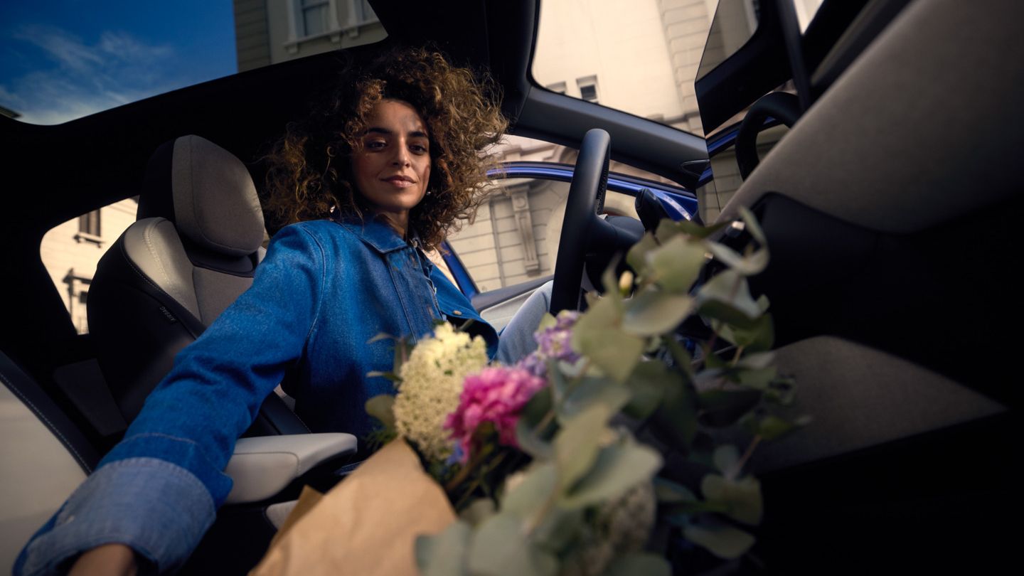 Uma mulher sentada no banco do condutor de um VW ID. Polo, a pegar num ramo de flores no banco do passageiro.