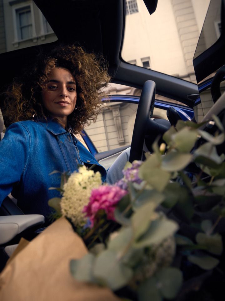 Uma mulher sentada no banco do condutor de um VW ID. Polo, a pegar num ramo de flores no banco do passageiro.