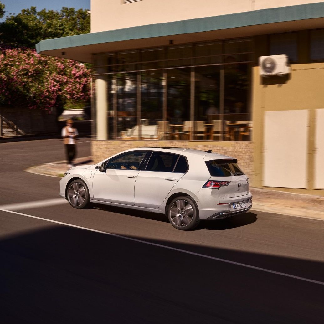 Weißer VW Golf wird an einer Ladestation geladen. Zwei Männer haben sich neben dem Auto in den Armen.
