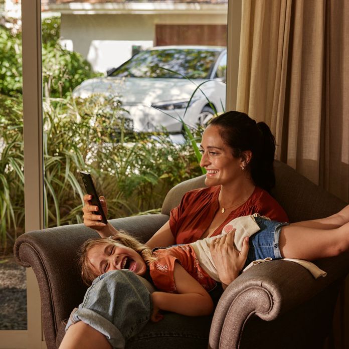 Eine Frau mit ihrer Tochter auf einem Sofa, die Frau blickt auf ihr Smartphone