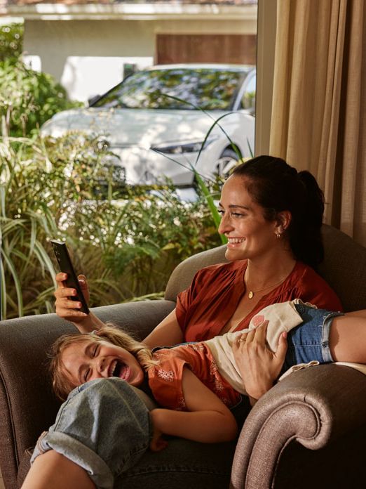 Eine Frau mit ihrer Tochter auf einem Sofa, die Frau blickt auf ihr Smartphone