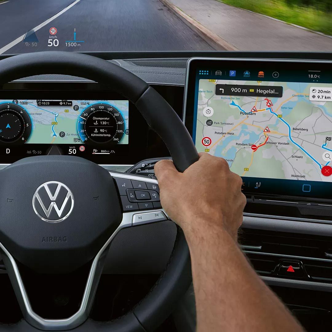 Vista interior do VW Passat focada no lado do condutor com um grande ecrã a cores e o head-up display. Duas mãos agarram o volante. 