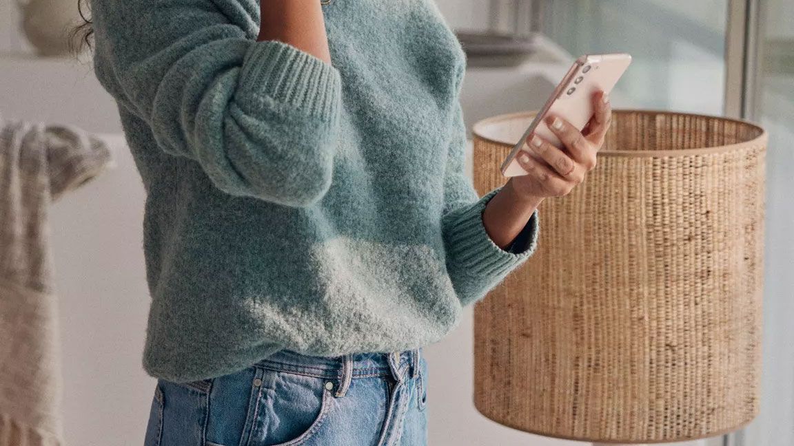 Uma mulher na sala de estar a olhar para o seu smartphone.