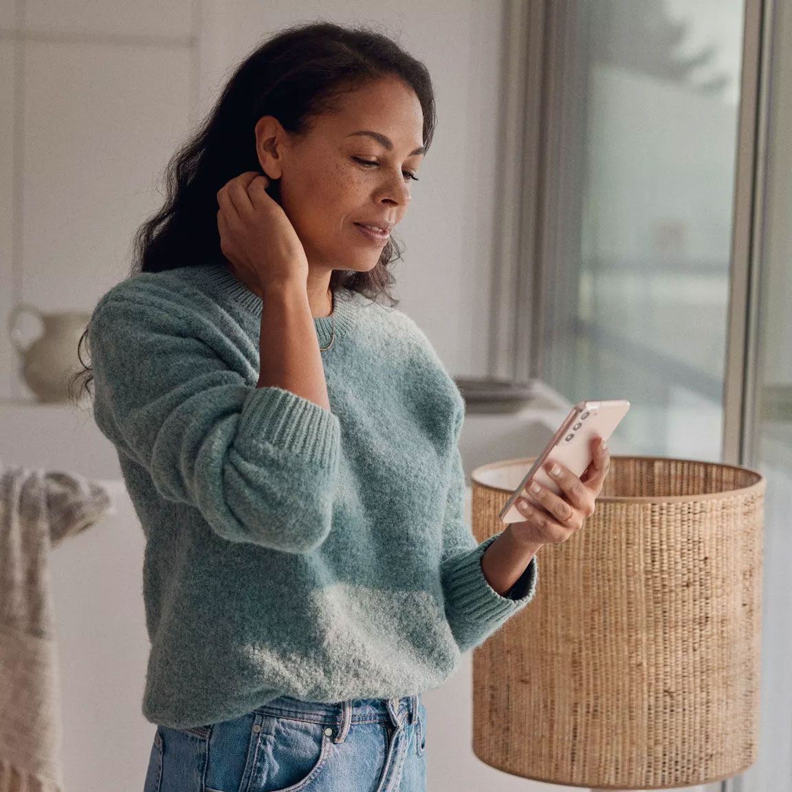 Uma mulher na sala de estar a olhar para o seu smartphone.