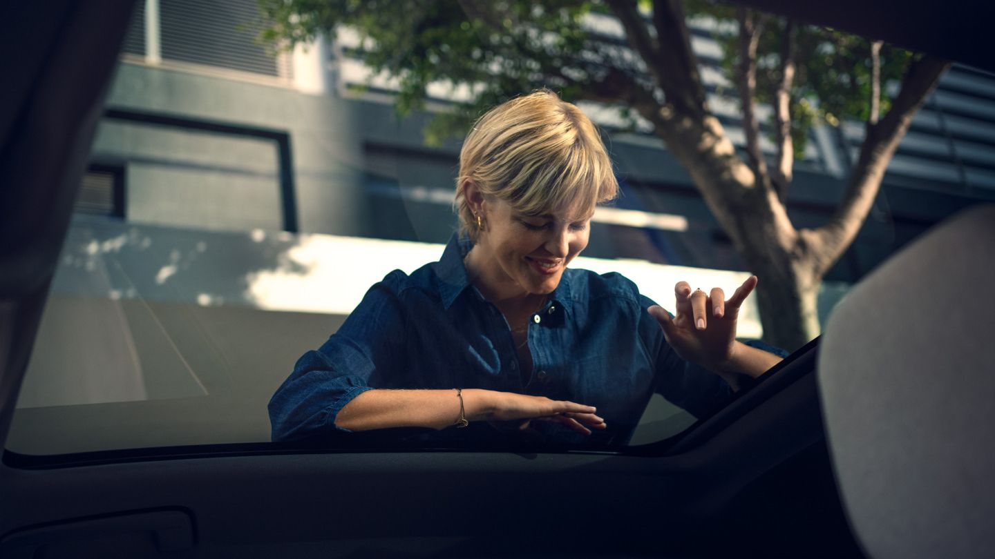 Uma mulher olha através do teto panorâmico de vidro para dentro de um VW ID. Polo e acena a alguém.