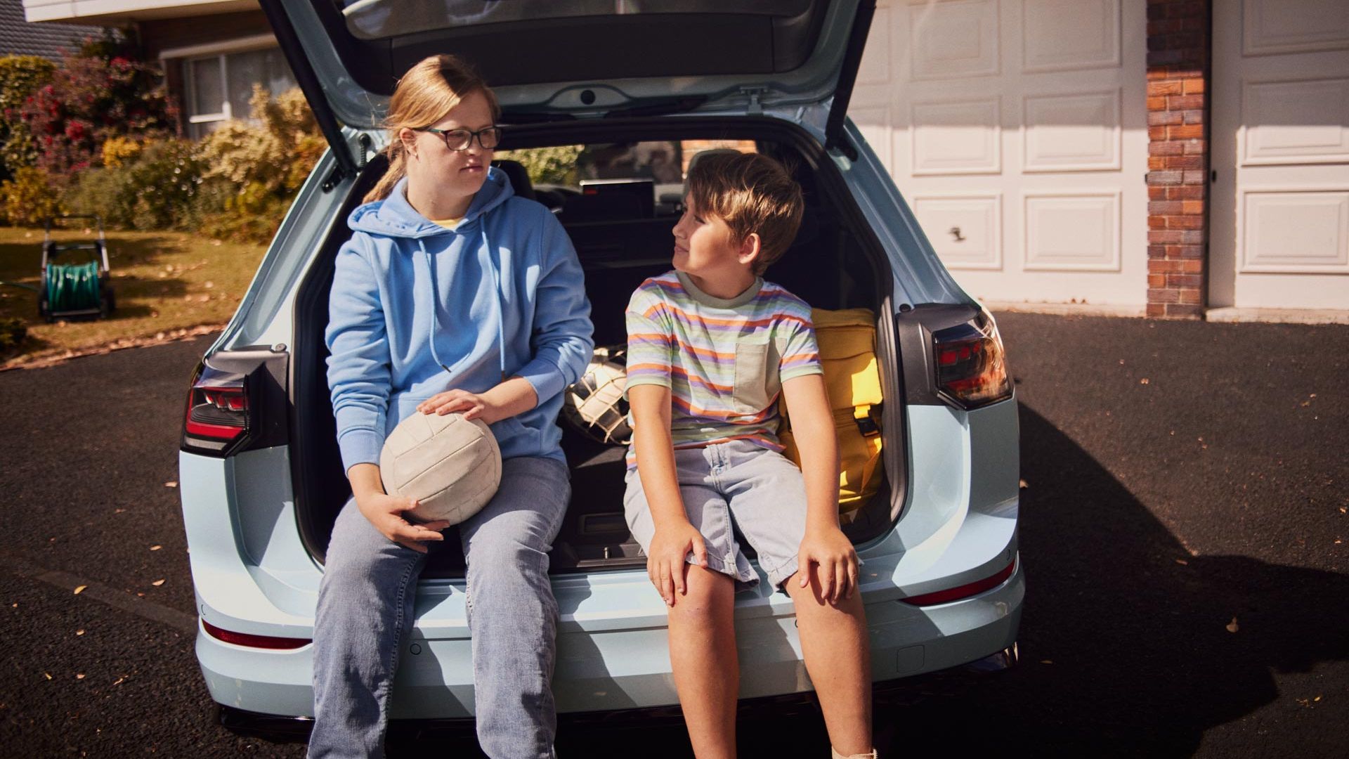 Ein Junge und ein Mädchen sitzen im Kofferraum eines weißen VW Golf Variant.
