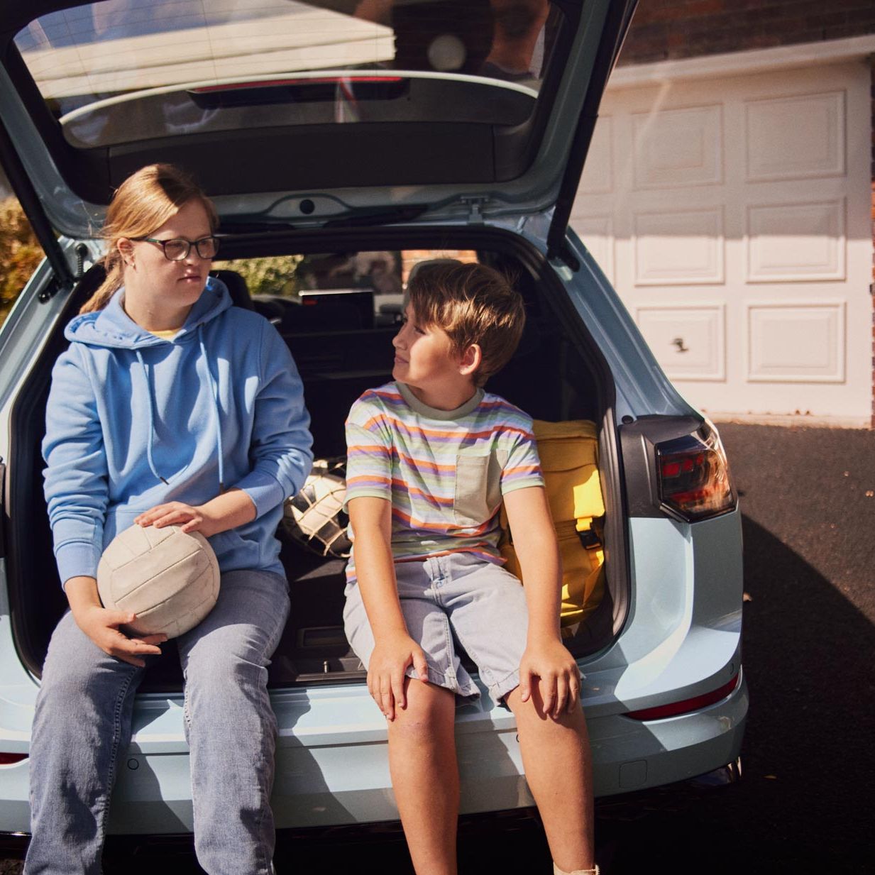 Ein Junge und ein Mädchen sitzen im Kofferraum eines weißen VW Golf Variant.
