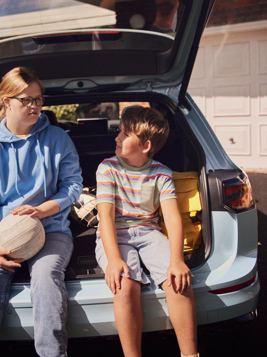 Ein Junge und ein Mädchen sitzen im Kofferraum eines weißen VW Golf Variant.