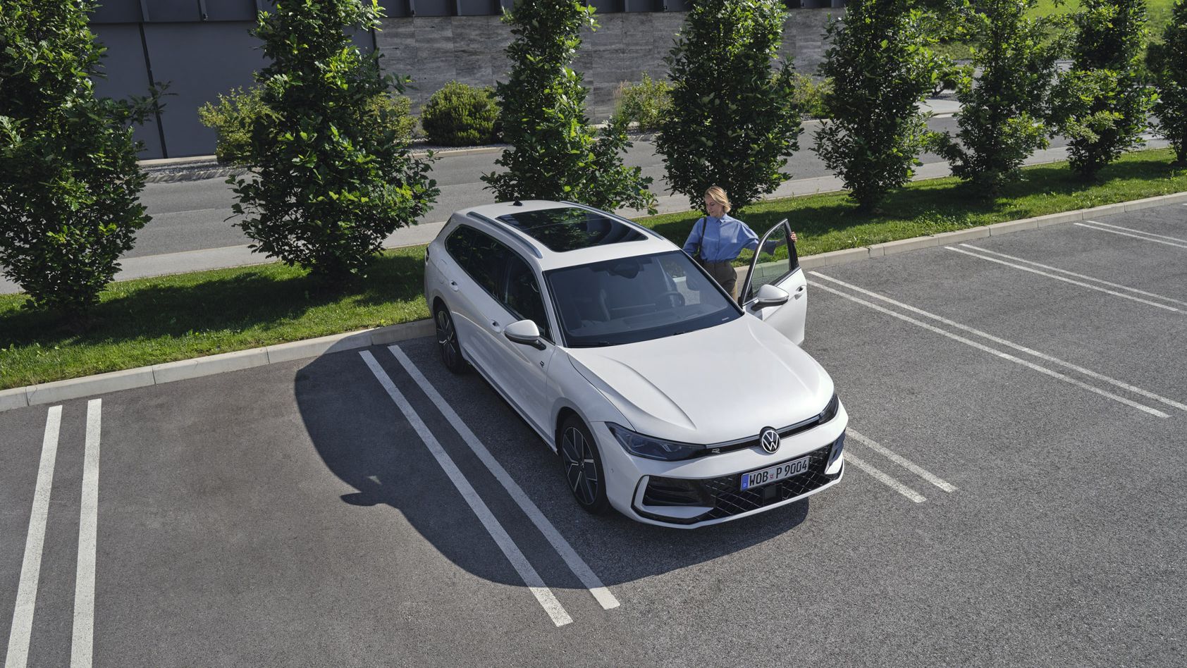Fotografia de cima de um VW Passat branco num parque de estacionamento, uma mulher entra no lado do condutor.