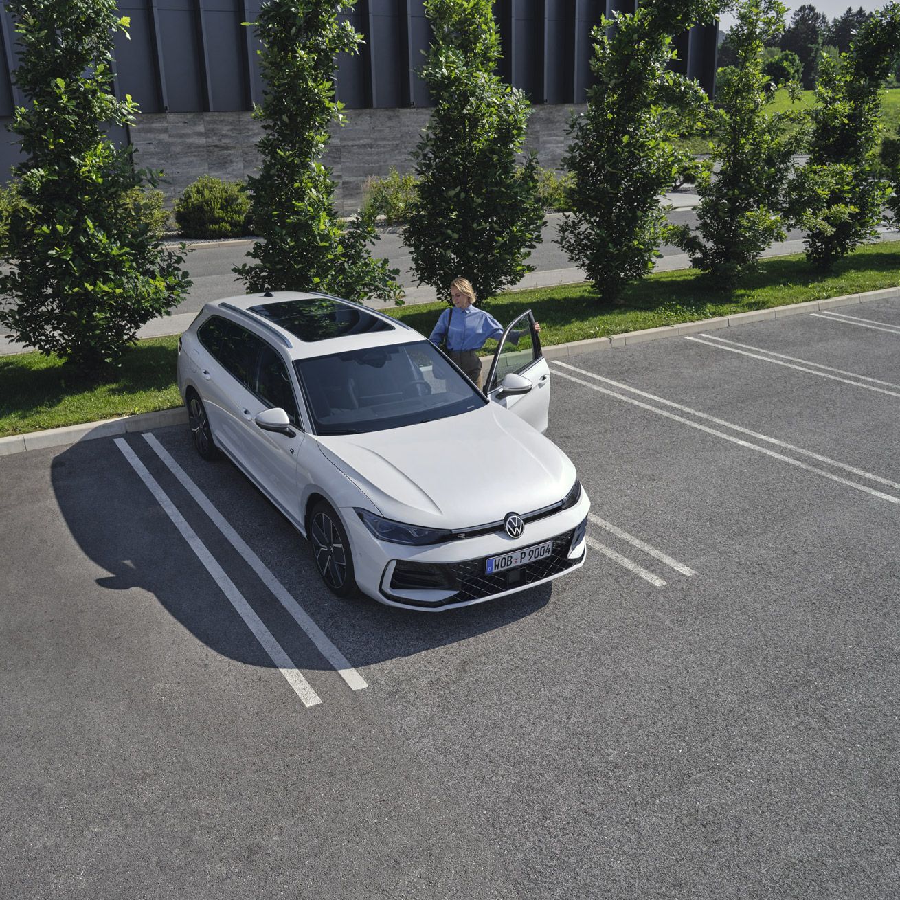 Fotografia de cima de um VW Passat branco num parque de estacionamento, uma mulher entra no lado do condutor.