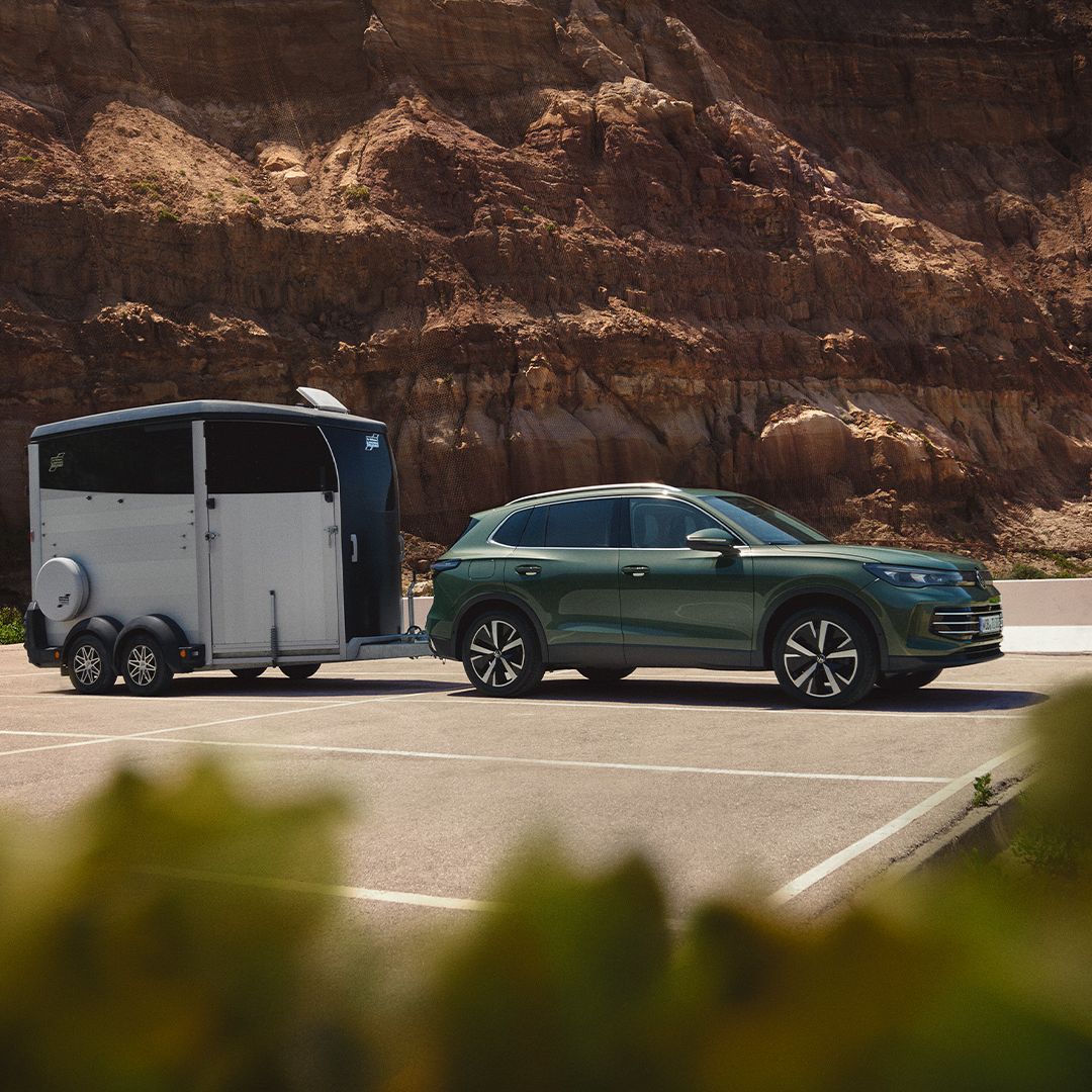VW Tiguan verde escuro com reboque para cavalos estacionado diante de uma paisagem rochosa.