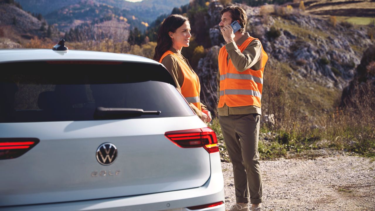 Duas pessoas com coletes de segurança laranja, ao lado de um carro da Volkswagen