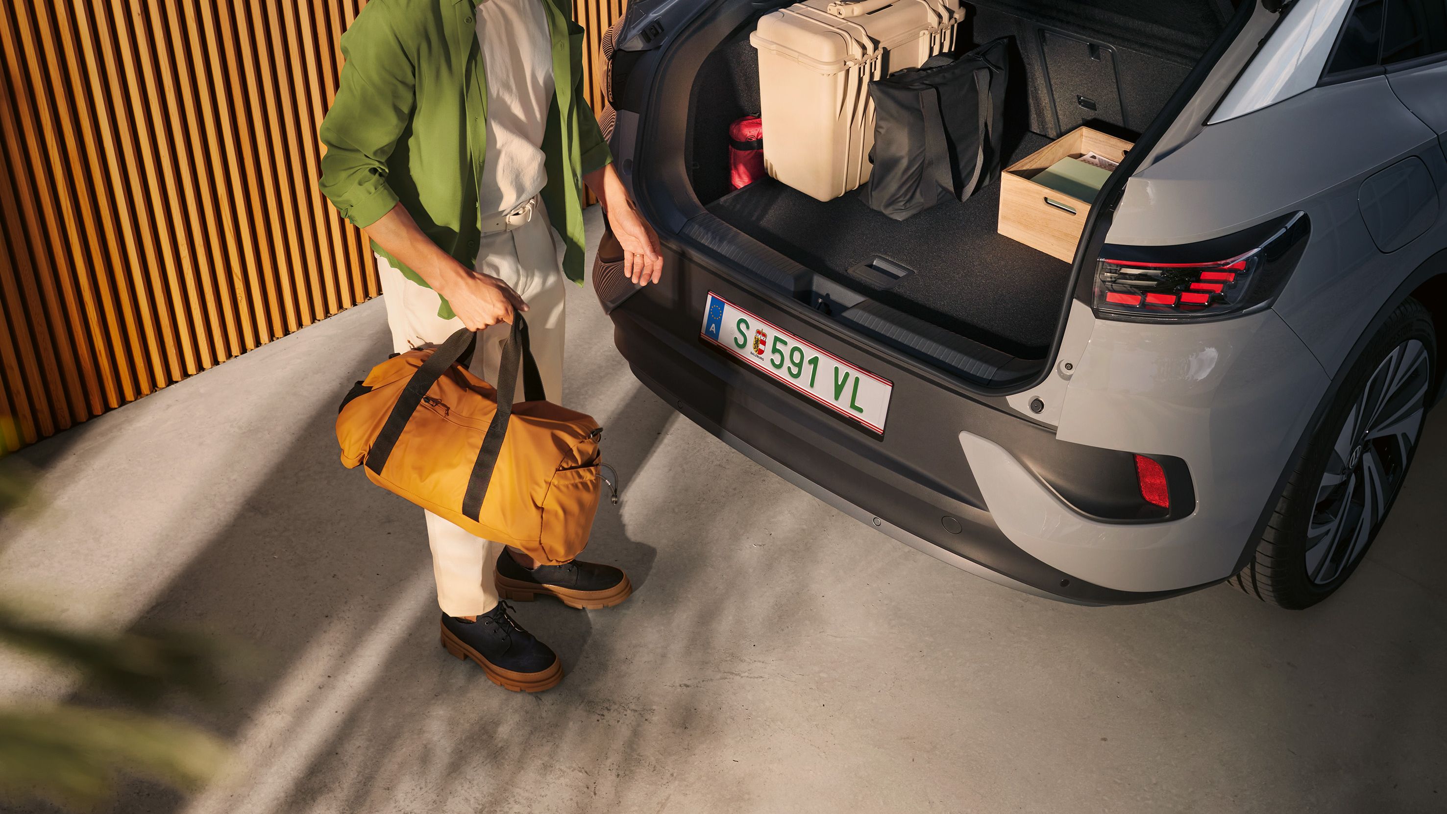 VW ID.5 com bagageira aberta e bagagem no interior, sob a tampa da bagageira aberta vê-se um homem de pasta na mão