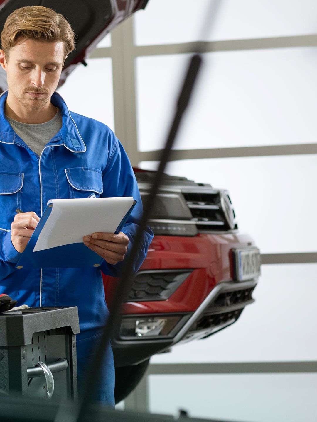Um empregado de serviço VW está a consultar uma lista de verificação em frente de um VW Tiguan Allspace vermelho