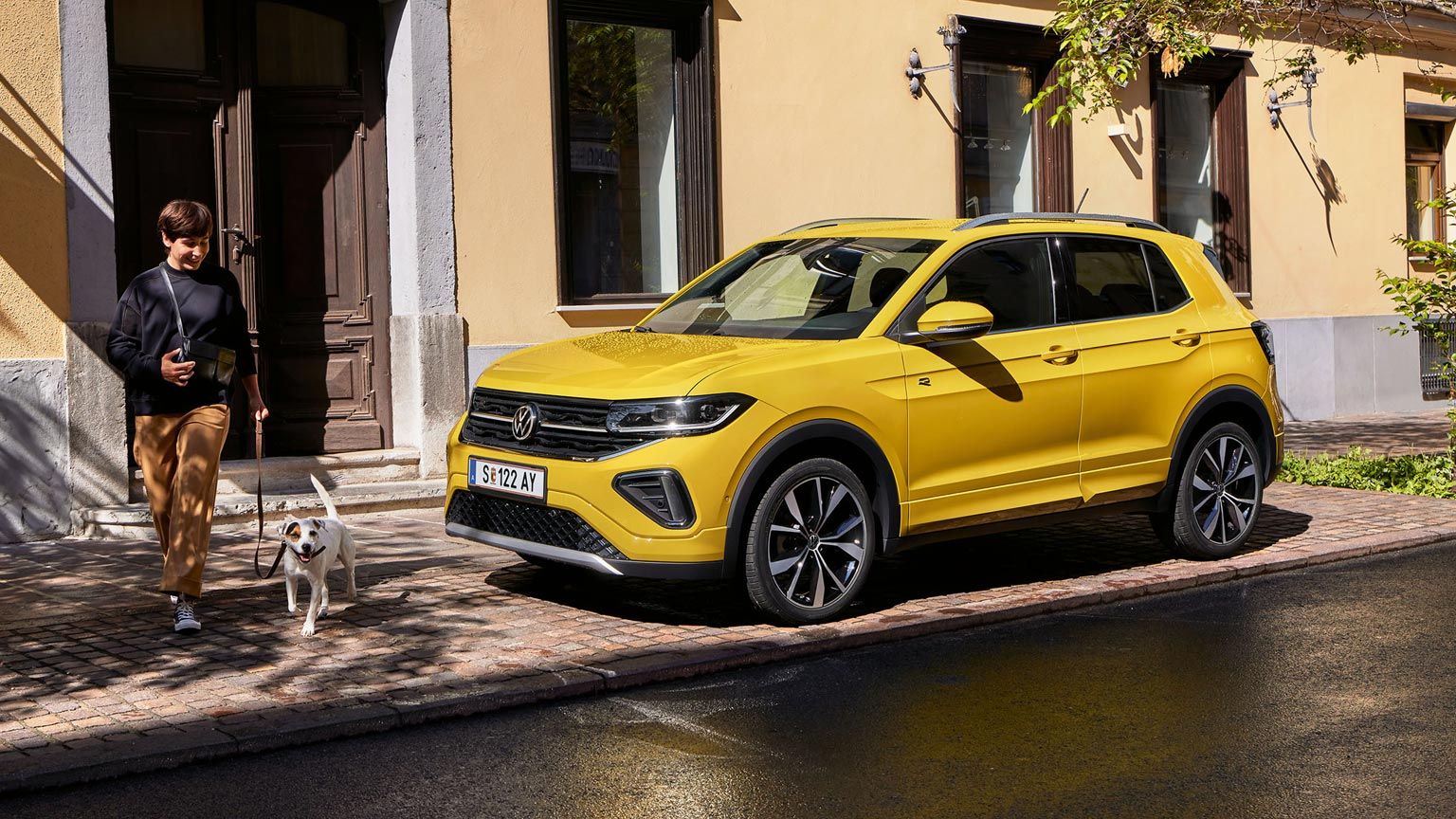 VW T-Cross parkt am Straßenrand, Frau mit kleinem Hund geht an ihm vorbei