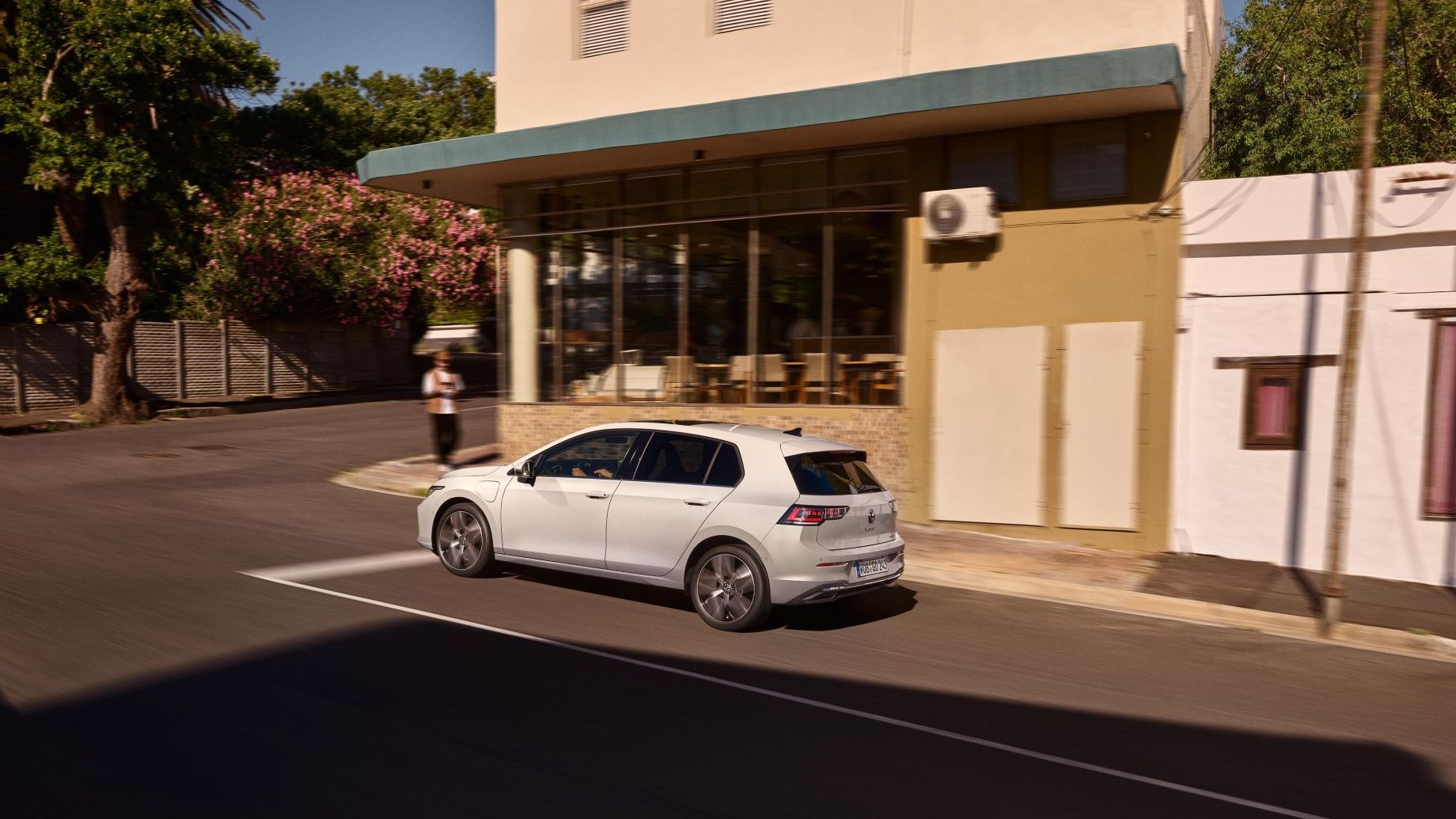 Weißer VW Golf wird an einer Ladestation geladen. Zwei Männer haben sich neben dem Auto in den Armen.
