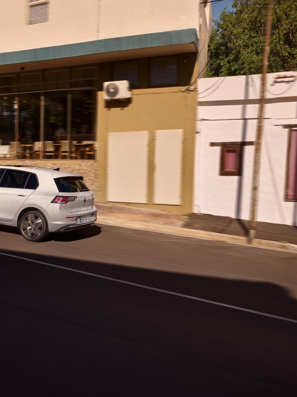 Weißer VW Golf wird an einer Ladestation geladen. Zwei Männer haben sich neben dem Auto in den Armen.