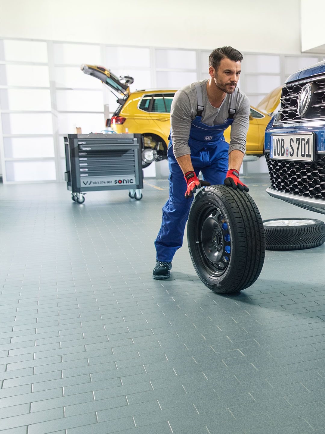 Dois empregados do serviço VW trabalham juntos na troca de pneus de um VW Tiguan azul numa oficina