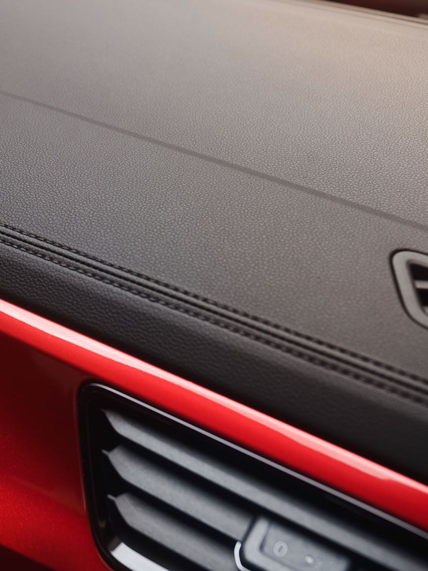 Interior do T-Roc Cabrio: Vista do ecrã com a exibição do menu e o volante multifunções. Uma mulher está de pé, à frente do Cabrio. 