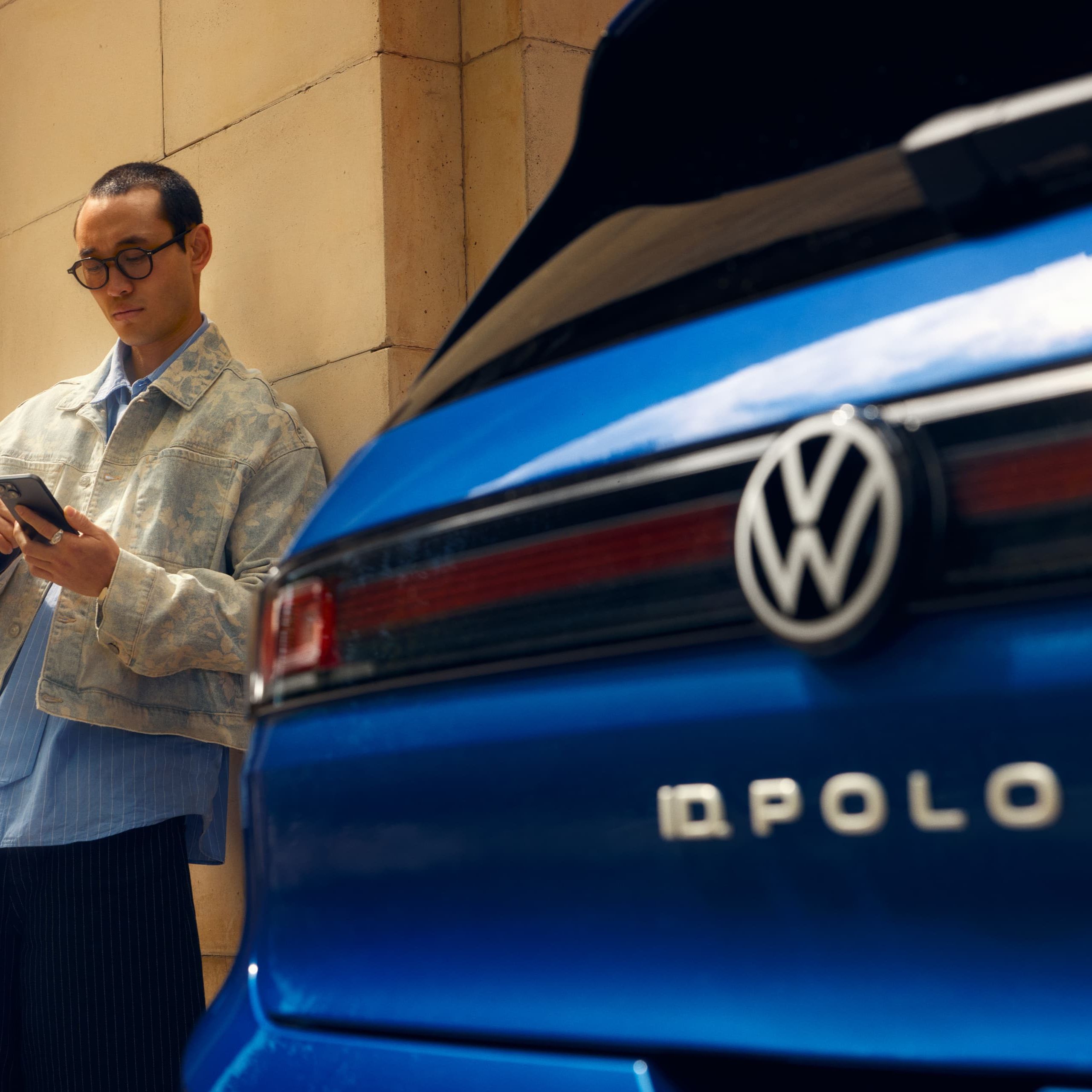 Vista traseira de um VW ID. Polo, com um homem de pé ao seu lado a usar o telemóvel.