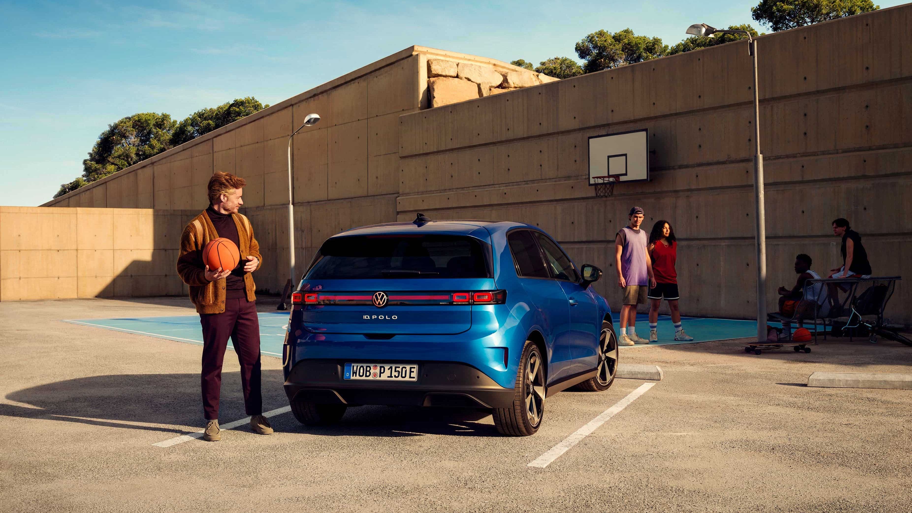 Um VW ID. Polo estacionado em frente a um campo de basquetebol. Um homem está ao lado dele, a segurar uma bola de basquetebol.