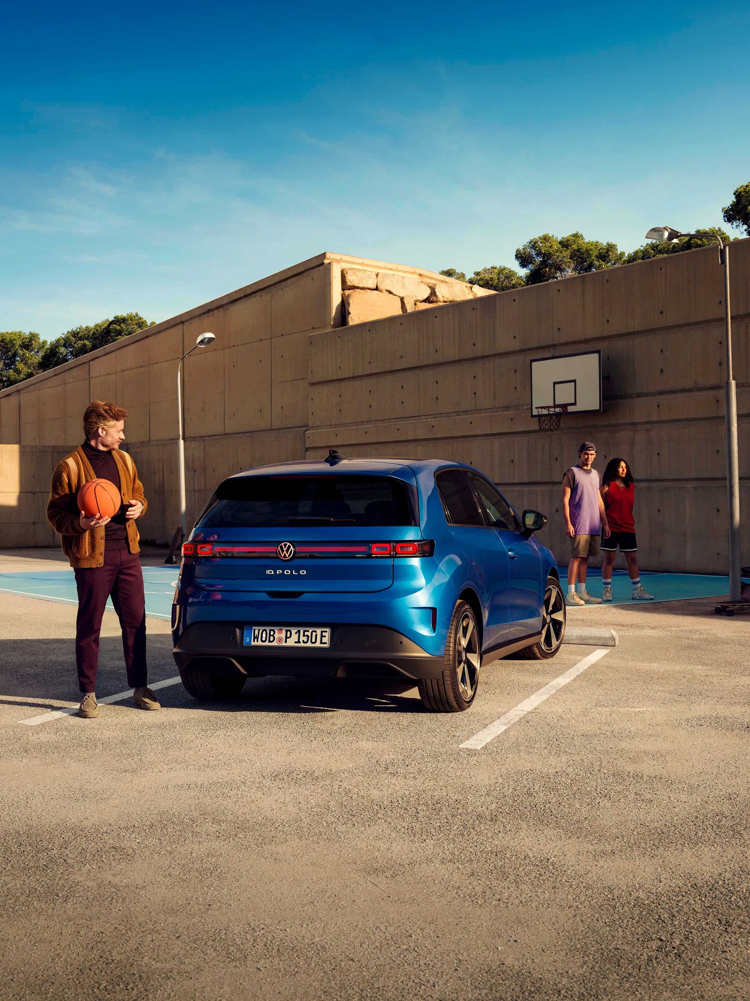 Um VW ID. Polo estacionado em frente a um campo de basquetebol. Um homem está ao lado dele, a segurar uma bola de basquetebol.