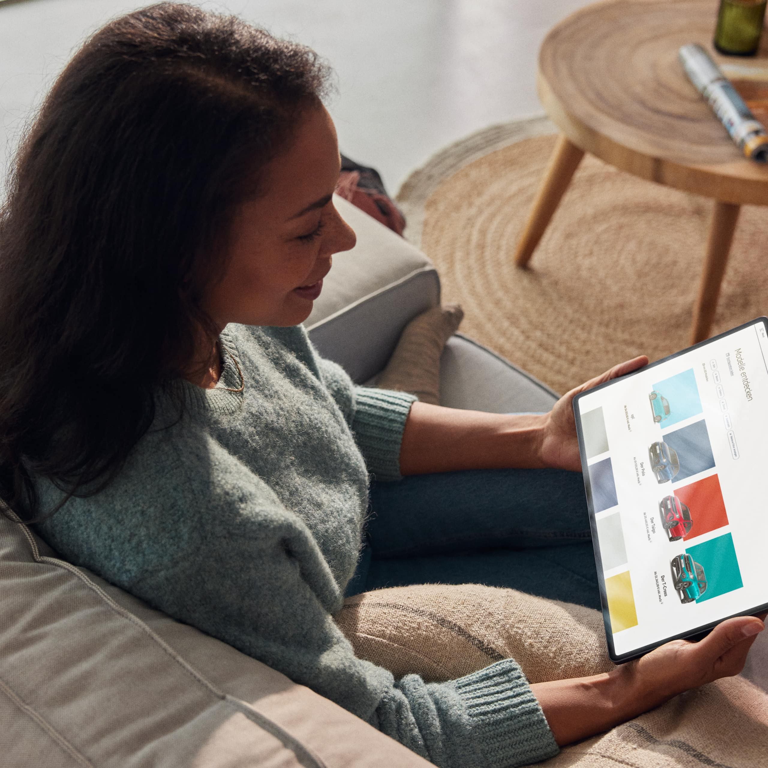 Mulher sentada num sofá com um tablet a pesquisar modelos no site VW.
