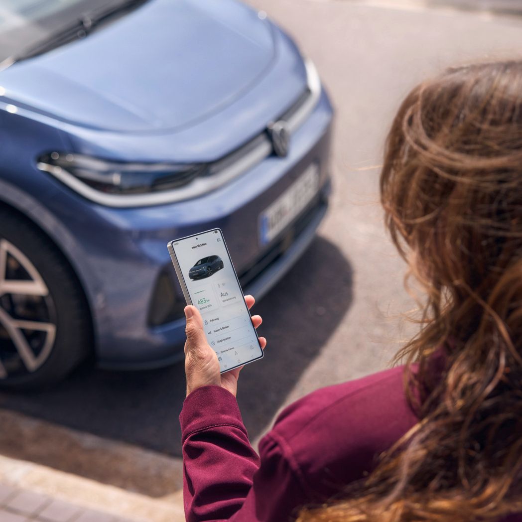 Eine Frau schaut auf ihr Smartphone, vor ihr parkt ein blauer VW ID.3 Neo