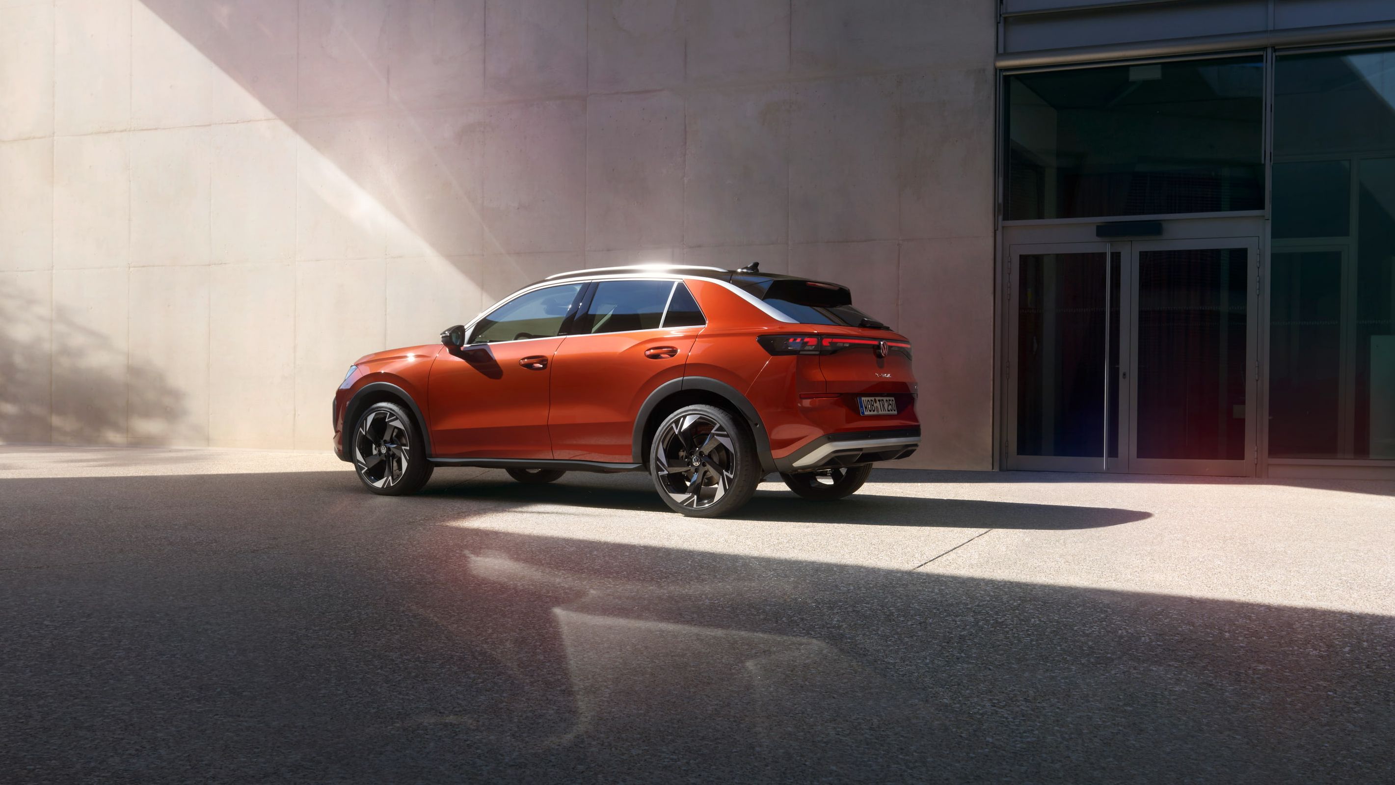 Um VW T-Roc Style vermelho está estacionado em frente a um edifício moderno.