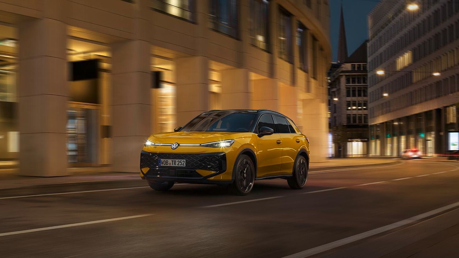 Um VW T-Roc R-Line amarelo atravessa um ambiente urbano à noite.