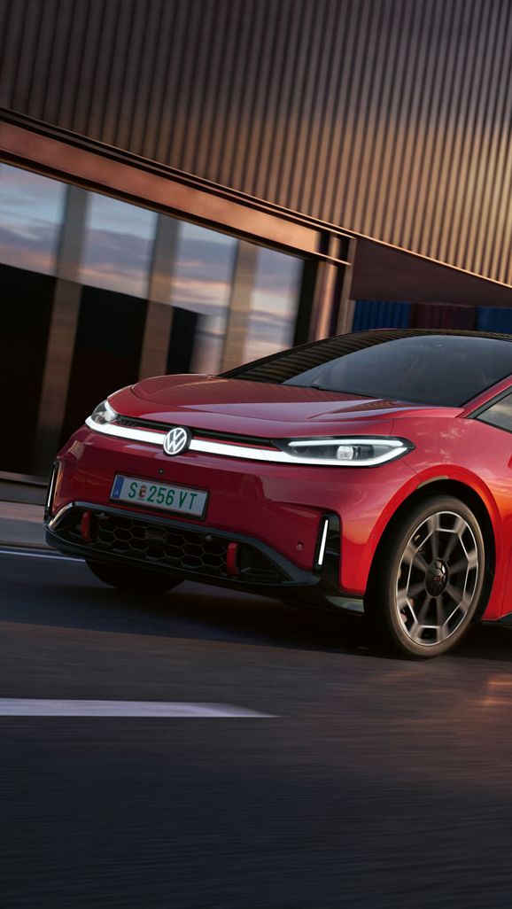 [AI-modified] – Um VW ID.3 GTI vermelho passa por um edifício portuário com os faróis ligados e o logótipo iluminado.