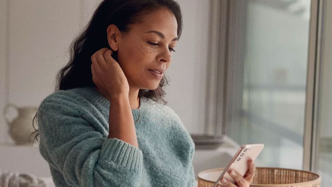 Uma mulher na sala de estar a olhar para o seu smartphone.